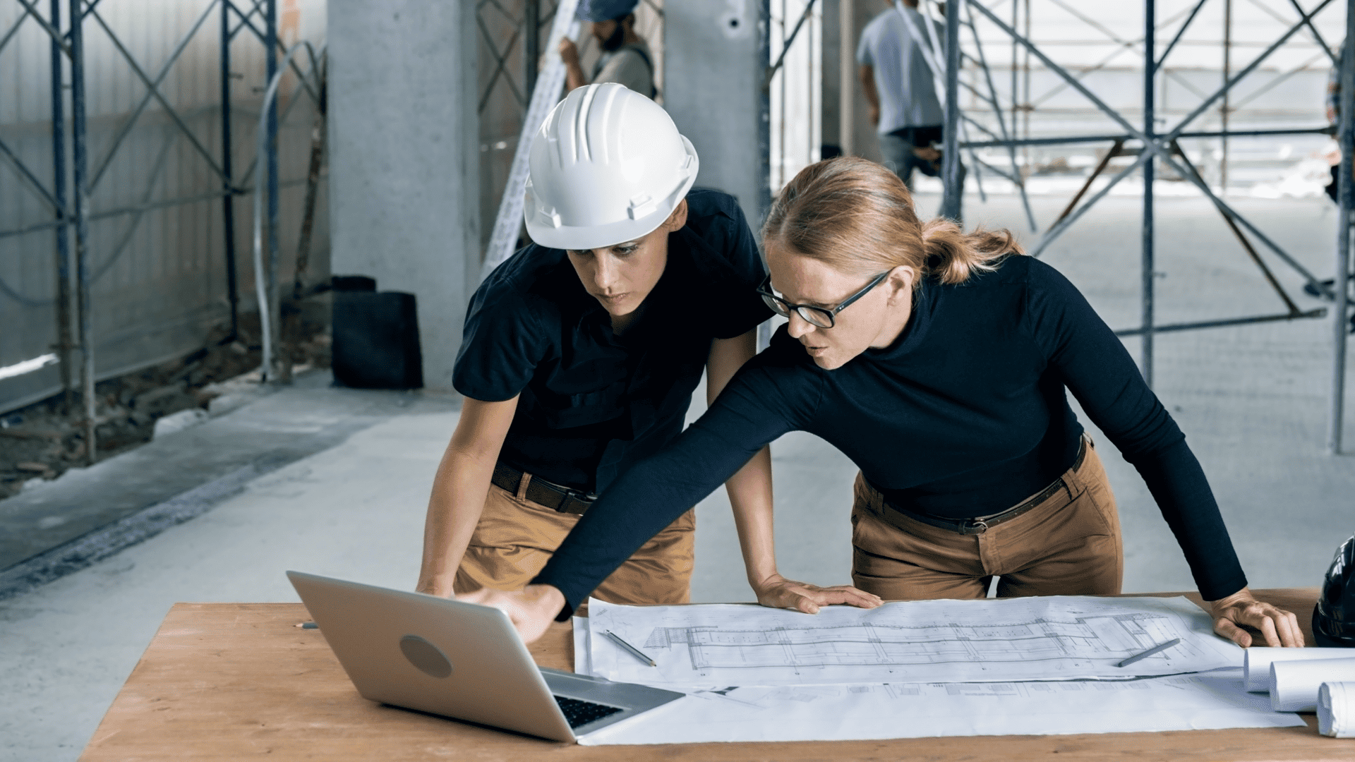 two women standing over a desk, looking at a laptop screen
